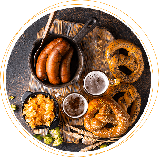 A rustic spread with sausages in a skillet, pretzels, beer, and sauerkraut, complemented by hops and wheat on a wooden board.